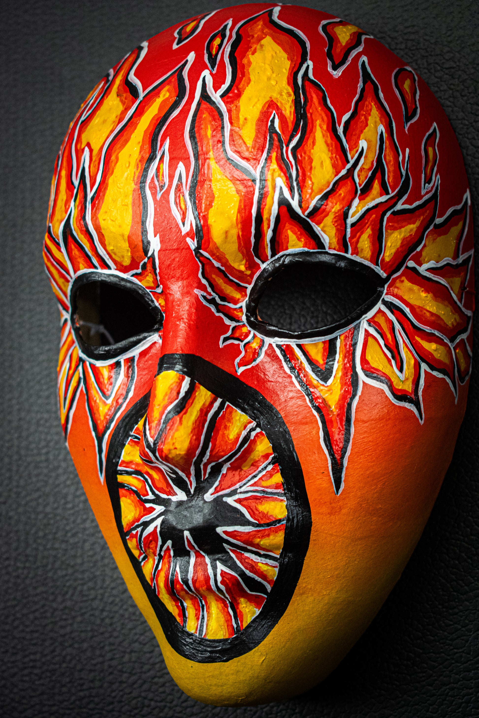 Masque artisanal orange avec motifs noir peints à la main.
